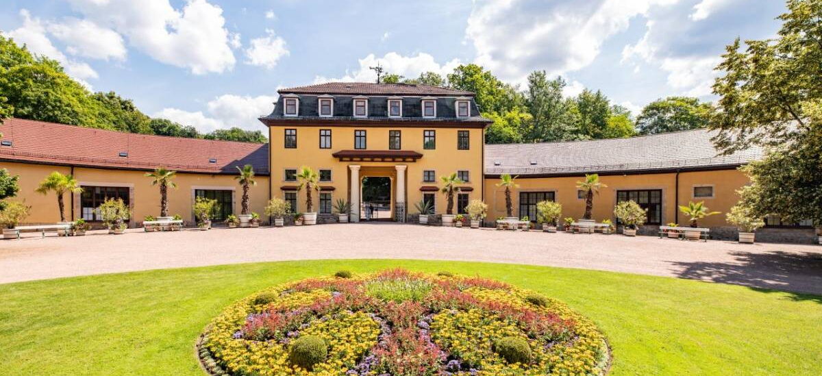 Landschaftsaufnahme mit Hofmarschallamt und kleinem bepflanzten Teppichbeet im Schlosspark Altenstein